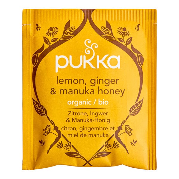 A yellow box of Pukka Organic Lemon, Ginger, and Manuka Honey Tea Bags on a table.