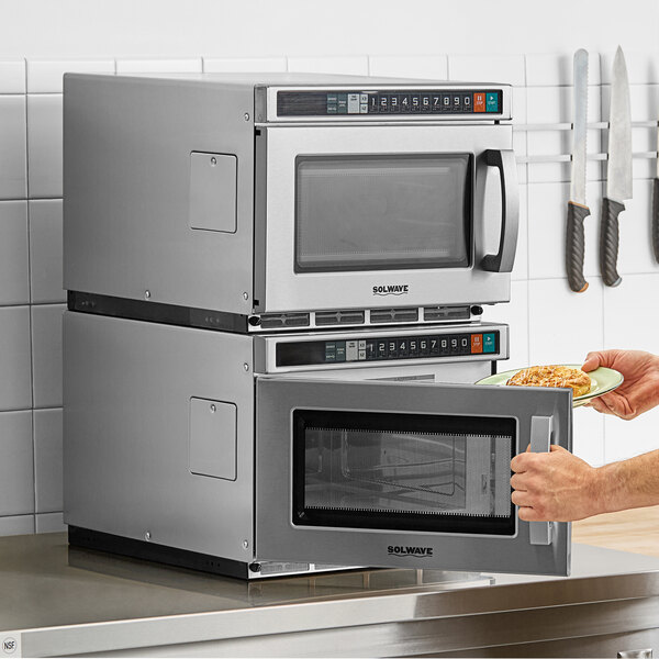 A person holding a plate of food opening a Solwave commercial microwave.
