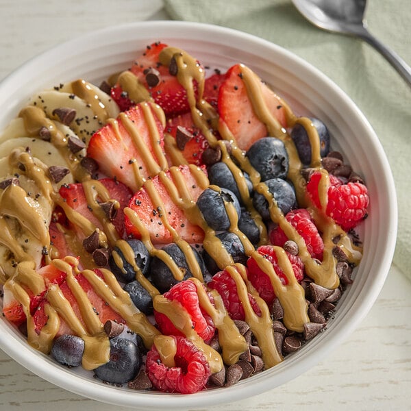 A bowl of fruit with a spoon and Producers Peanut Company Natural Creamy Peanut Butter.