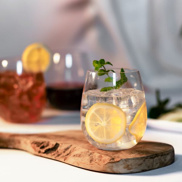 A Carlisle stemless wine glass filled with ice water and lemon slices on a wooden board.