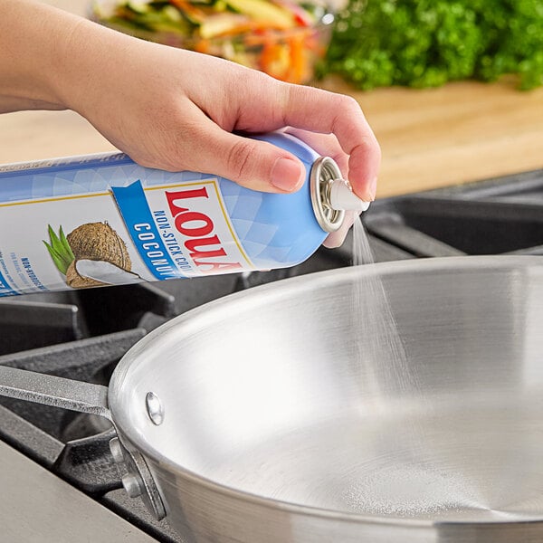 A hand using LouAna Non-Stick Coconut Oil Cooking Spray to grease a pan.