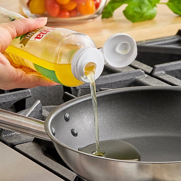 A person pouring LouAna Avocado Oil into a frying pan.