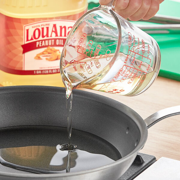 A person pouring LouAna High Performance Peanut Oil from a measuring cup into a pan.