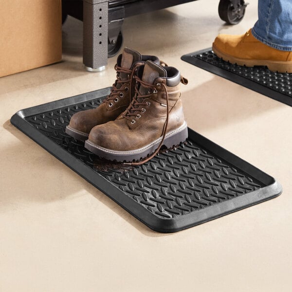 A black rubber boot tray with a diamond pattern, holding a pair of brown work boots.