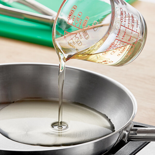 A person pouring LouAna Peanut Oil from a measuring cup into a pan on a stove.