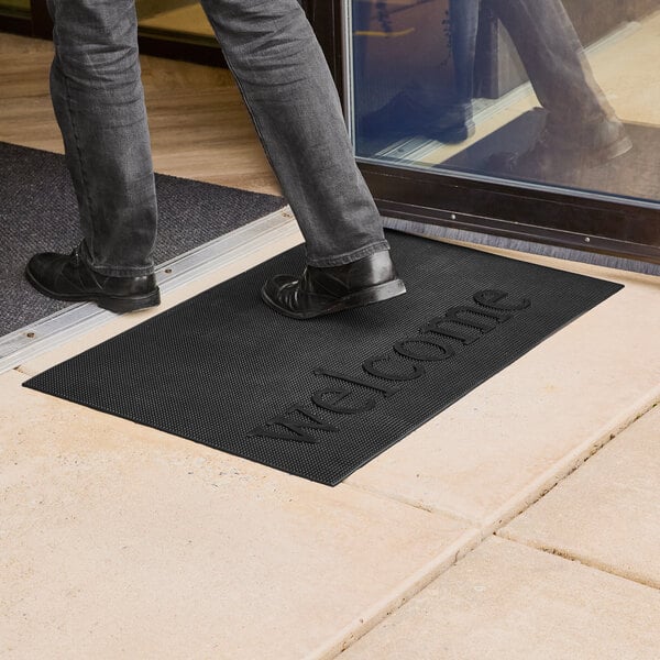 A black rubber entrance mat with the word 'welcome' embossed on it, placed at a doorway.