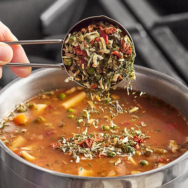 A person using a measuring cup to pour Silva Dried Soup Vegetable Blend into a bowl of soup.