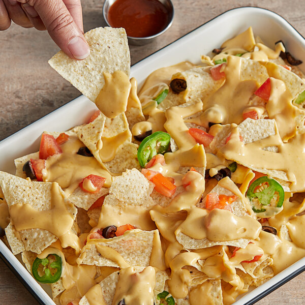 A person dips a chip into a bowl of WayFare Dairy-Free Vegan Nacho Cheddar Sauce.