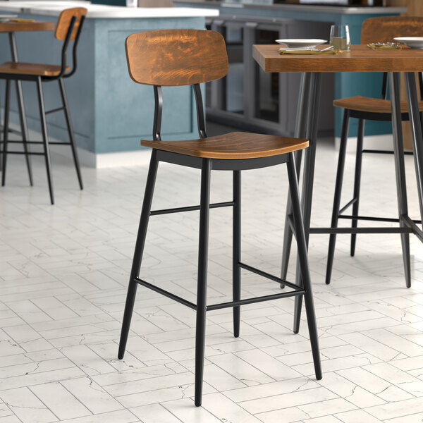 Three Lancaster Table & Seating black barstools with vintage wood seats at a table in a restaurant.