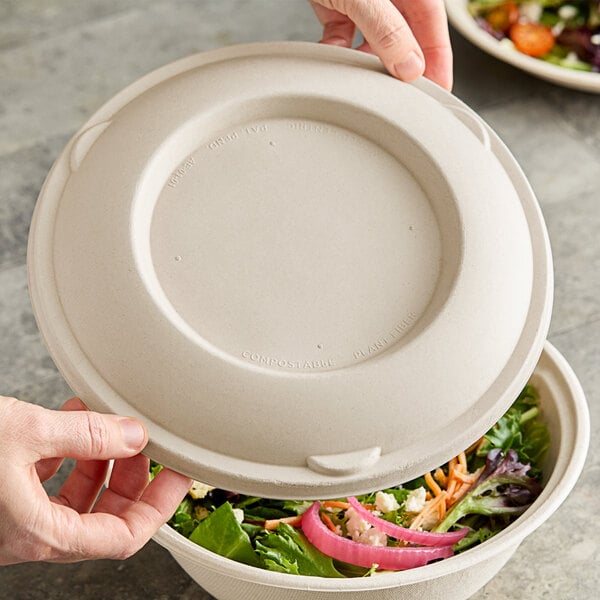 A person holding a World Centric compostable fiber bowl with a World Centric compostable fiber lid over a salad.