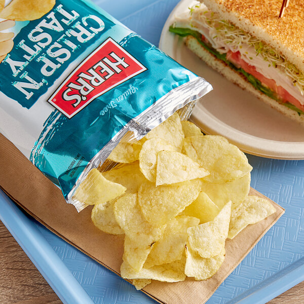 A plate with a sandwich and Herr's Crisp N' Tasty Potato Chips.