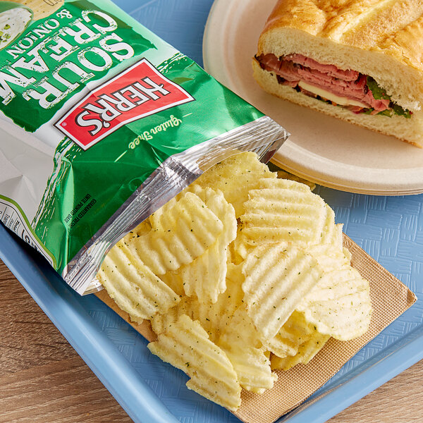 A plate with a sandwich and a bag of Herr's Sour Cream & Onion Potato Chips.