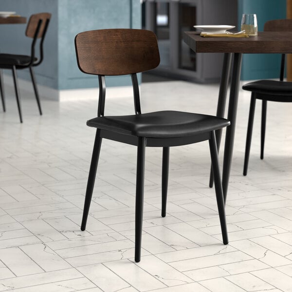 A Lancaster Table & Seating black chair with black vinyl padded seat and espresso wood backrest on a table in a restaurant dining area.