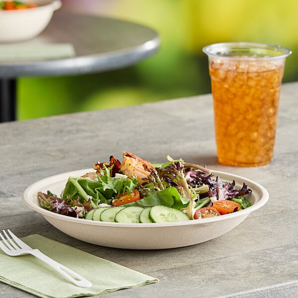 A World Centric compostable fiber bowl filled with salad on a table with a glass of iced tea.