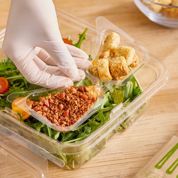 A hand in a glove putting food in an Inline Plastics 2-compartment tray insert inside a plastic container.