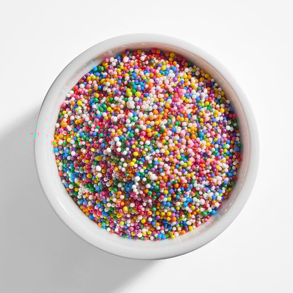 A white bowl filled with colorful rainbow nonpareil sprinkles.