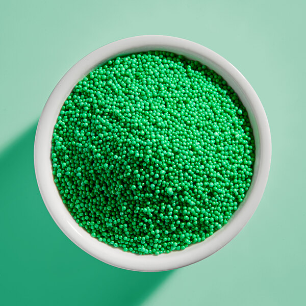 A white bowl filled with green nonpareil sprinkles.