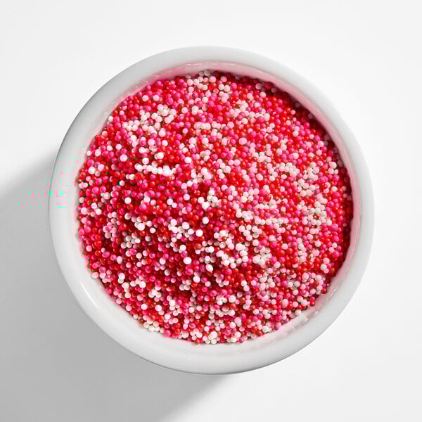 A bowl filled with a mix of red, pink, and white nonpareil sprinkles.