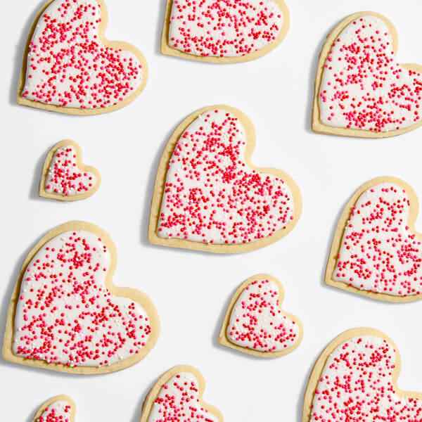 A selection of heart-shaped sugar cookies decorated with white icing and red nonpareil sprinkles.