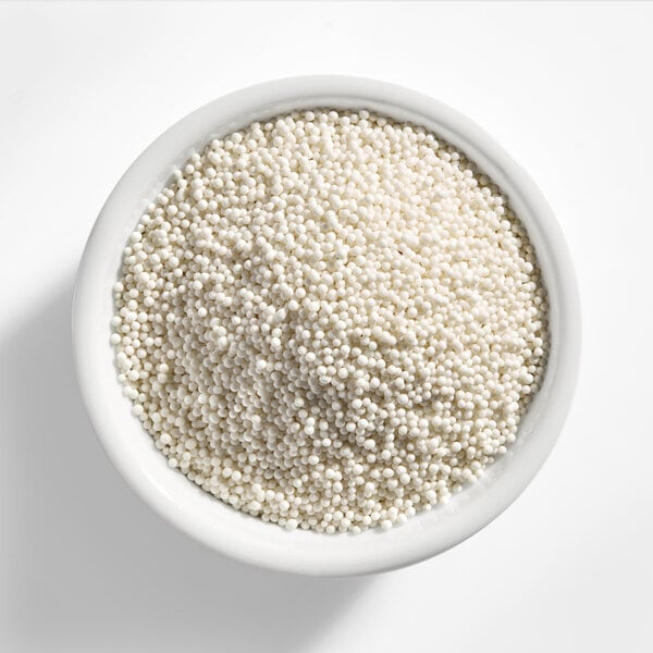 A white bowl filled with small white nonpareil sprinkles.