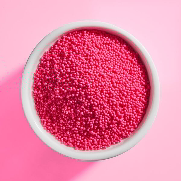 A white bowl filled with bright pink nonpareil sprinkles on a pink background.