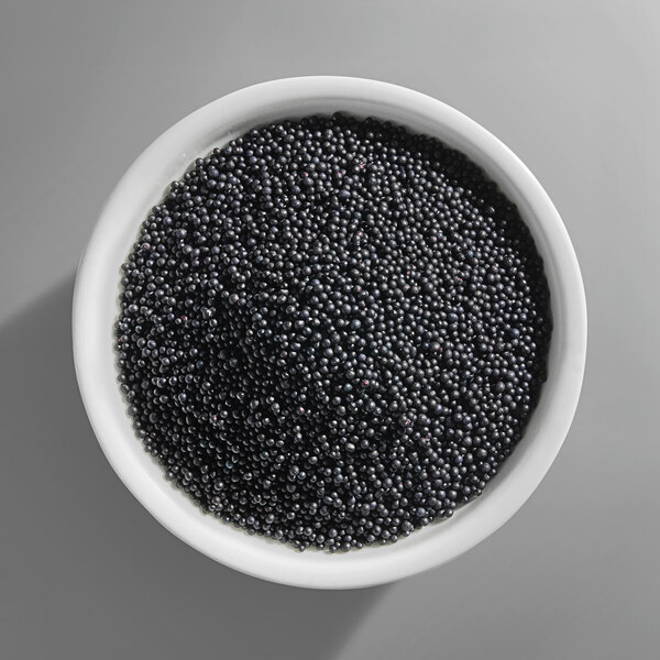 A white bowl filled with small black nonpareil sprinkles.