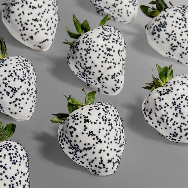 A group of strawberries coated in white chocolate and decorated with black nonpareil sprinkles.