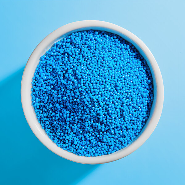 A white bowl filled with small, round, bright blue nonpareil sprinkles.