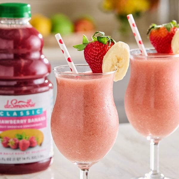Two glasses of pink strawberry banana smoothies with straws and fruit.
