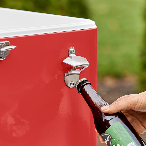 A hand opening a bottle of beer with a Choice red steel beverage cooler.