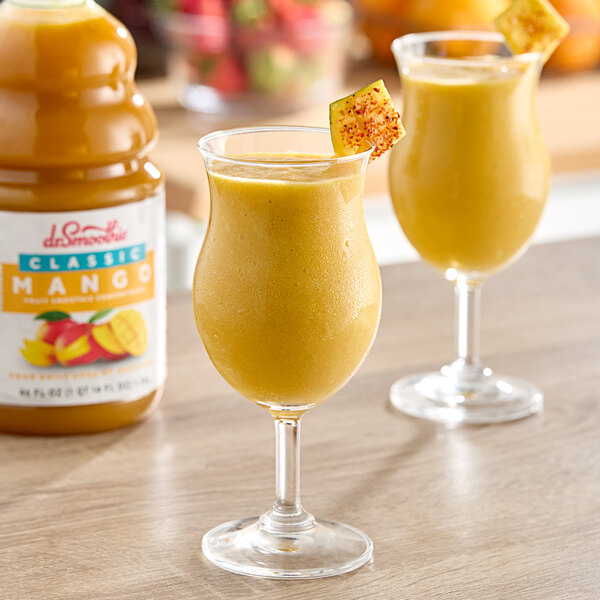 Two glasses of yellow Dr. Smoothie Classic Mango fruit smoothie on a table.