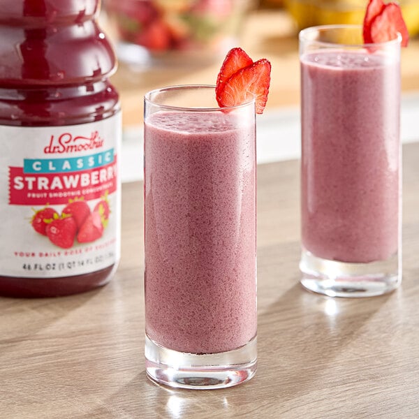 Two glasses of pink Dr. Smoothie Classic Strawberry smoothie with strawberries on top.