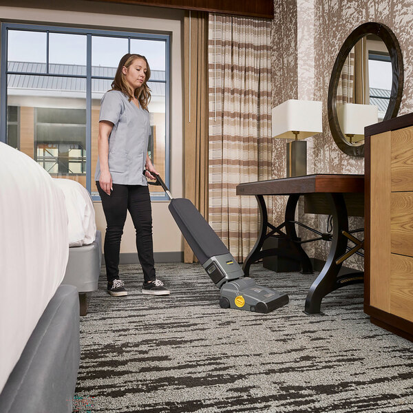 A woman using a Karcher cordless upright vacuum in a hotel room.