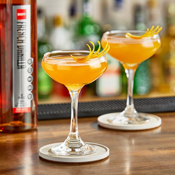 Two glasses of orange drinks with SHOTT French Vanilla syrup on a bar counter.