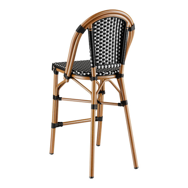 A Lancaster Table & Seating black and white checkered rattan bar stool on an outdoor patio.