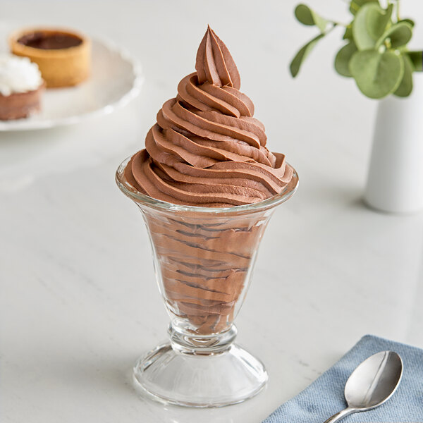 A glass cup filled with Eclipse Foods chocolate soft serve ice cream with a spoon in it.