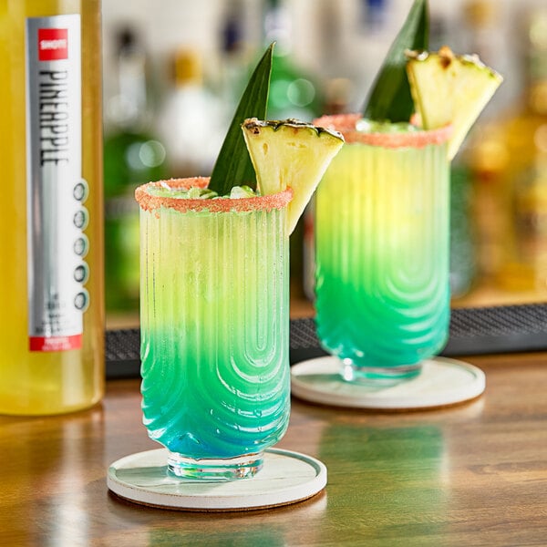 Two drinks with pineapple garnish on a bar counter.