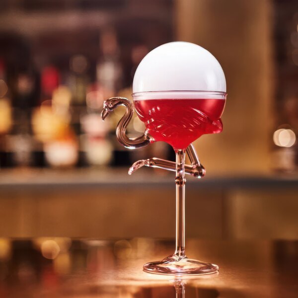 A Flamingo Cocktail glass filled with a red cocktail on a bar counter.