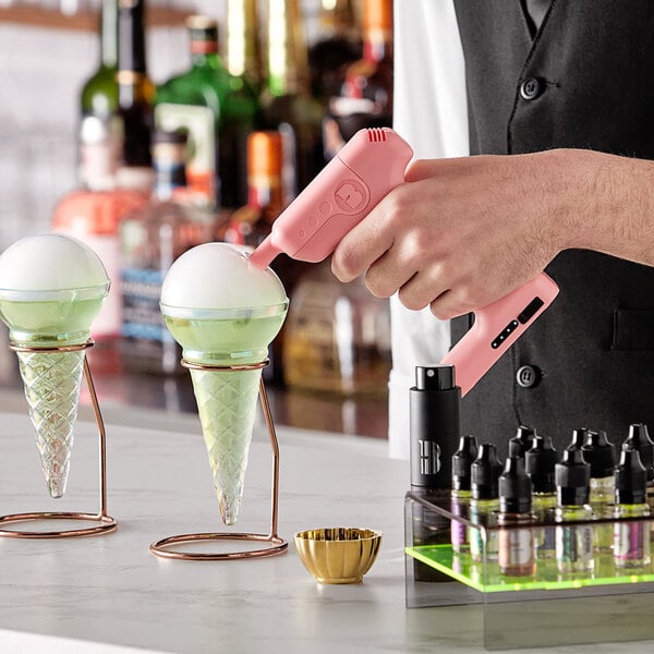 A person holding a pink Flavour Blaster device over ice cream cones in glass cones.