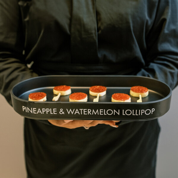 A woman holding a Cal-Mil black melamine low rim platter with appetizers.