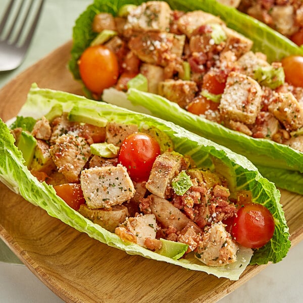 A wooden plate with lettuce wraps filled with Brakebush Farm Pantry boneless skinless halal chicken breast chunks and vegetables.