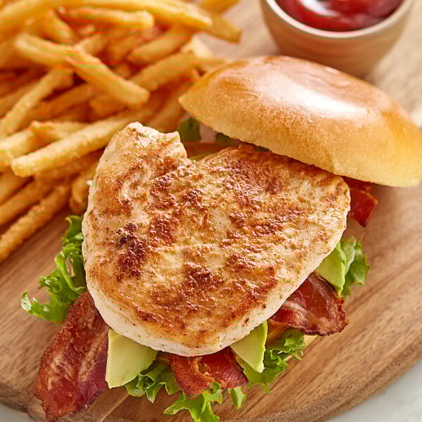 A chicken sandwich with bacon and lettuce served with fries on a wooden board.