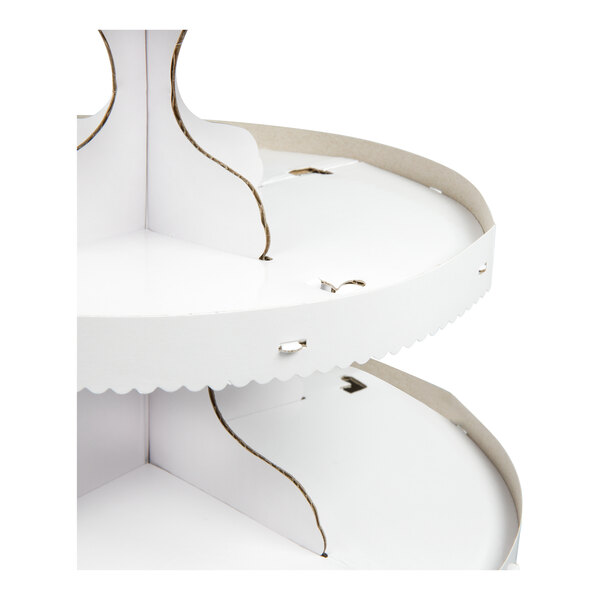 A close-up view of a white, three-tiered cardboard stand with scalloped edges and visible assembly slots.