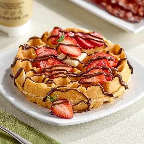 A waffle with strawberries and Lindt hazelnut chocolate sauce drizzled on top.