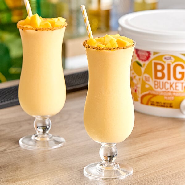 Two glasses of yellow Master of Mixes Mango Daiquiri on a table with straws.