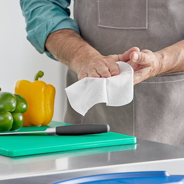 A man using WipesPlus Lemon Scent hand sanitizing wipes on a cutting board in a professional kitchen.