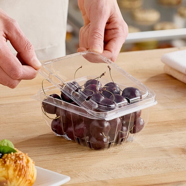 A person's hands using a plastic clamshell to put cherries in it.