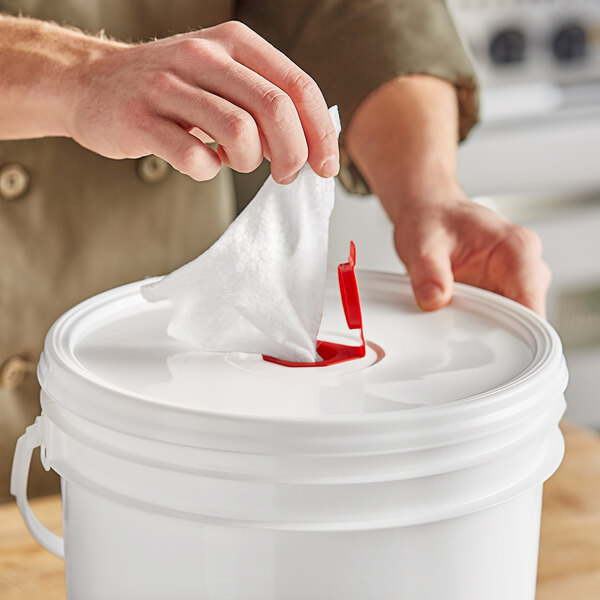 A hand pulling a WipesPlus hand sanitizing wipe from a white bucket.