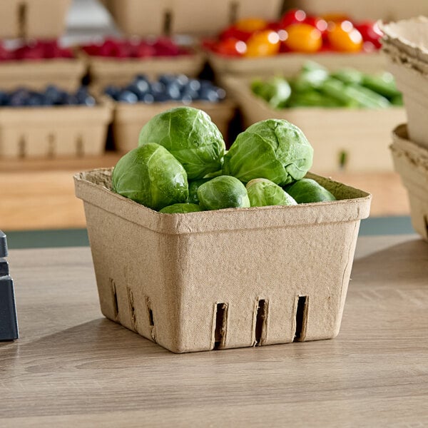 A close up of a cardboard Choice Produce Basket filled with brussels sprouts on a table.
