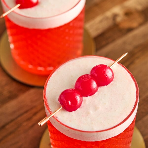 A glass of red beverage garnished with three maraschino cherries on a skewer.